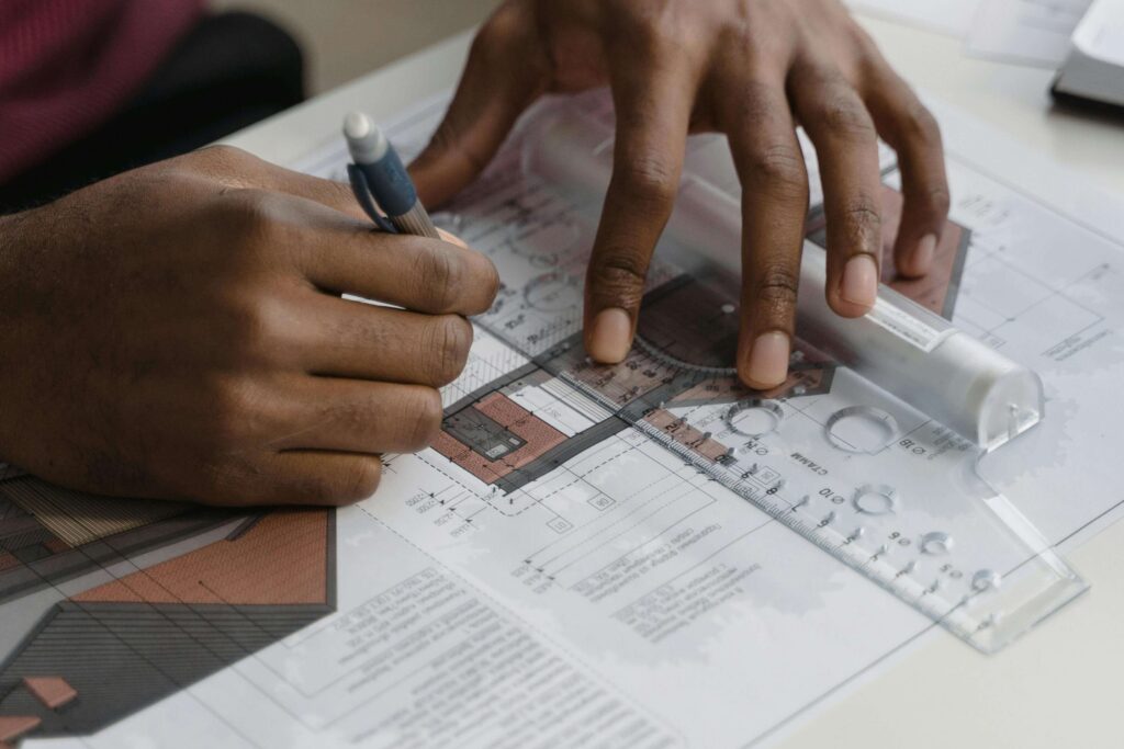 Hands drawing blueprints with a pen and ruler.