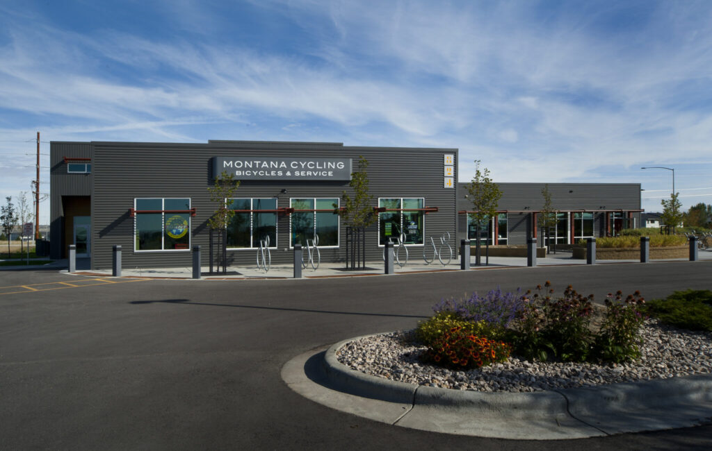 Montana Cycling store with a sleek, modern exterior, large windows, bike racks, and a well-maintained parking area under a clear blue sky.