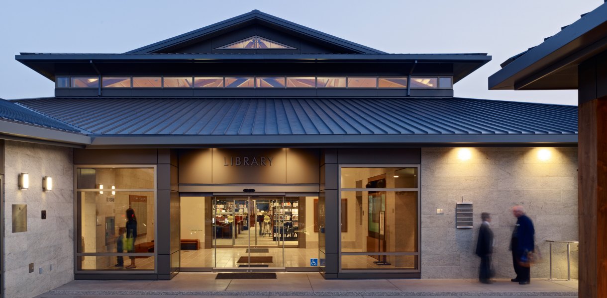 Lafayette Library and Learning Center with a metal roof and glass entrance, illuminated in the evening.