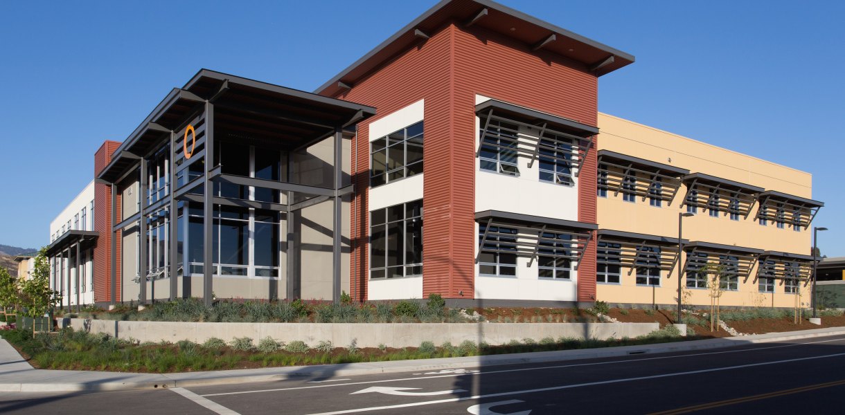 Office building with red and beige panels, large windows, and metal framework at MindBody Headquarters.