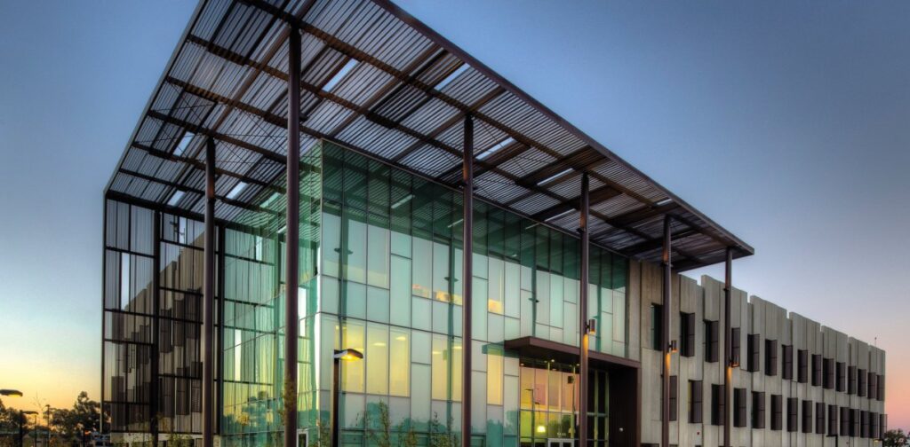 Office building with glass facade, metal overhang, and evening lighting at UC San Diego East Campus.