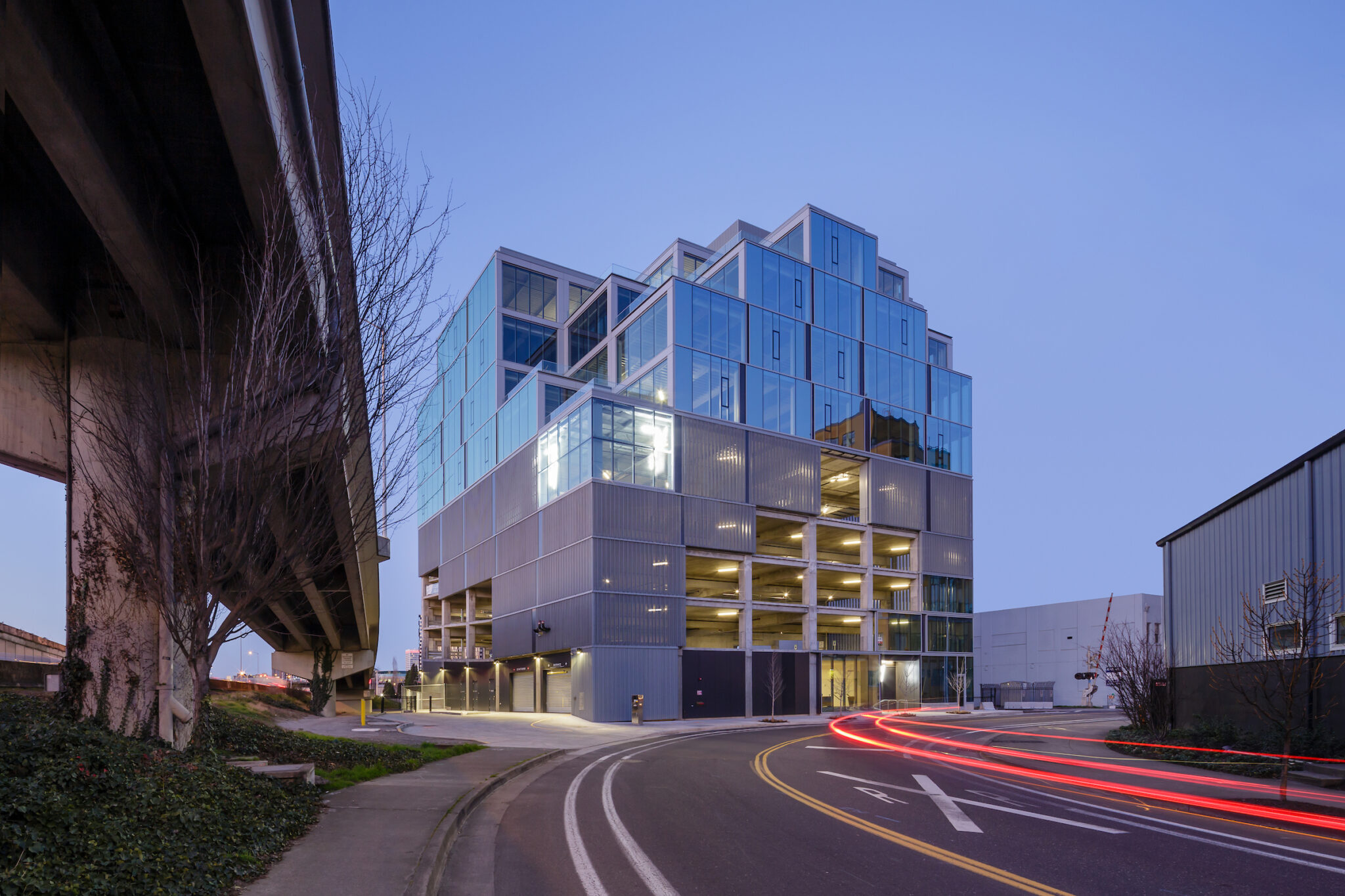 Prefabricated metal office retail complex with modern design elements. The 7 Stark Building at dusk next to an onramp for the neighboring highway in Portland, Oregon. Car tail lights streak by in the foreground.