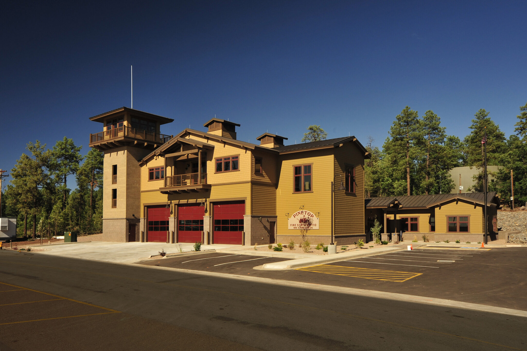 Pinetop Fire Station 110 with a brown exterior and red garage doors, surrounded by trees."