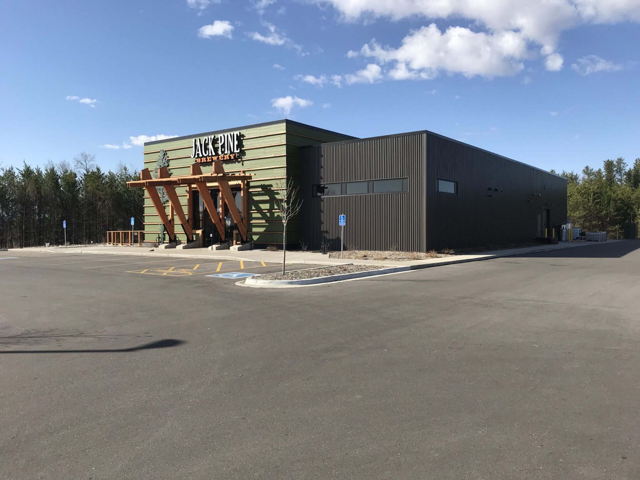 Jack Pine Brewery restaurant building with a contemporary design, metal siding, green and brown exterior, and prominent wooden beams at the entrance.