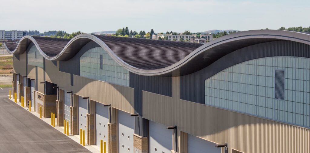 Spokane International Airport Snow Removal Facility with wave-like roof design, featuring garage doors and a large, paved area.